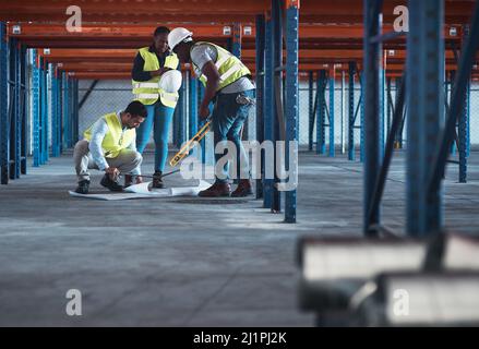 We speak engineer fluently. Shot of a group of contractors using a blueprint to plan in the warehouse. Stock Photo