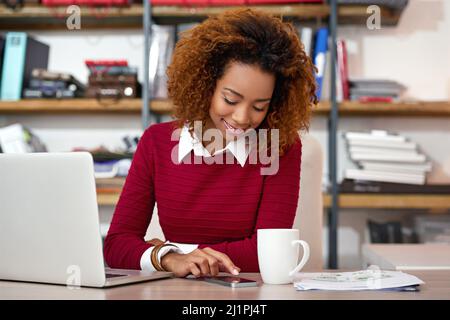 Checking her schedule for today. Shot of a young woman sending at text while working on a laptop in an office. Stock Photo