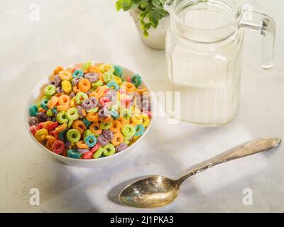 Colored fruit rings in a bowl, a spoon, a jug of milk and an indoor flower decor. Isolated on white background. Quick whole grain breakfast. Children' Stock Photo