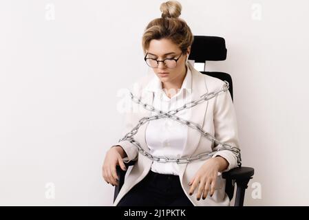 Upset business woman tied up to the office chair with a chains Stock Photo