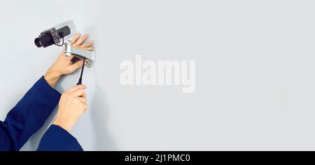 Copy space banner background with electrician repairing surveillance camera on white wall Stock Photo