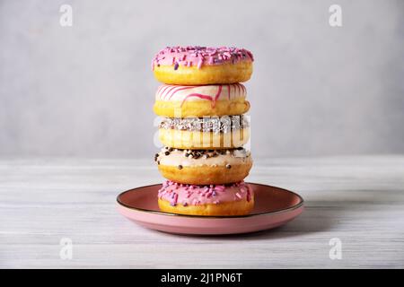 Stack of various colorful donuts on pink ceramic plate Stock Photo