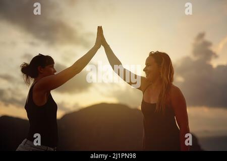 Best vacation ever. Shot of two happy young friends high fiving each other at sunset. Stock Photo