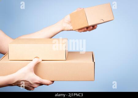 Stack of cardboard boxes in female hands. Blank parcel boxes on light blue background. Packaging, shopping, free shipping, delivery concept Stock Photo
