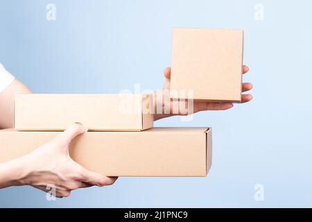 Stack of cardboard boxes in female hands. Woman showing small blank brown box. Blank parcel boxes on light blue background. Packaging, shopping, free Stock Photo