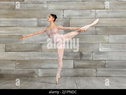 Full body of female classical ballet dancer balancing on tiptoes in pointe shoes during rehearsal in dance studio Stock Photo