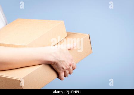 Stack of cardboard boxes in female hands. Blank brown parcel boxes on light blue background. Packaging, shopping, free shipping, delivery concept Stock Photo