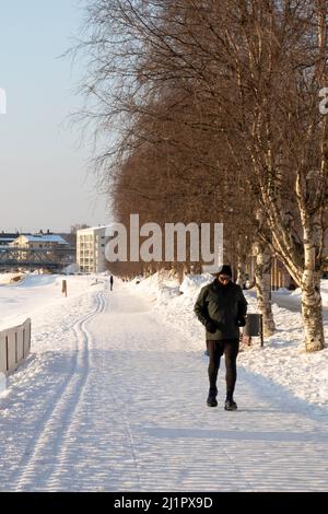 Rovaniemi, Finland - March 17th, 2022: A man jogging on a snowy road on the bank of the frozen Kemijoki river, Rovaniemi, Finland. Stock Photo