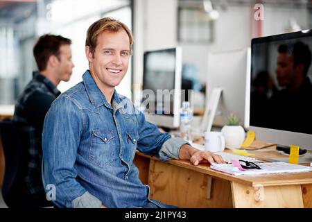 We design dreams here. Portrait of a designer sitting at his desk in an office. Stock Photo