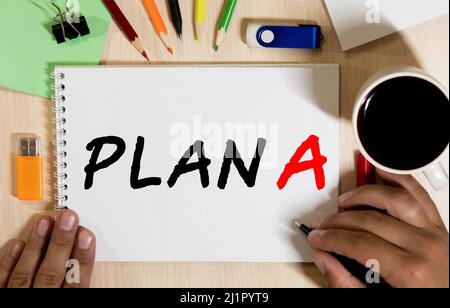 Plan A text with a person holding a pen on a wooden desk. Stock Photo