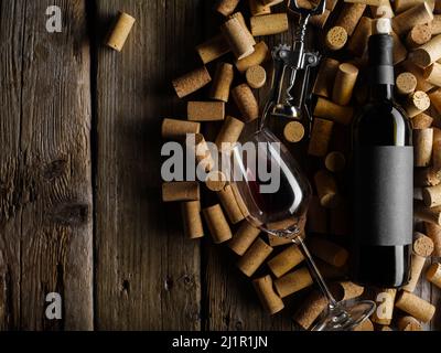Lots of wine corks, a bottle of red wine, a wine glass and a corkscrew. Isolated on a wooden background. Low angle view. There is free space to insert Stock Photo