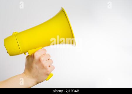 Yellow megaphone in a man's hand on a white background. Minimalism. Journalism, speaker, advertising, elections, rumors, fakes, false information. The Stock Photo