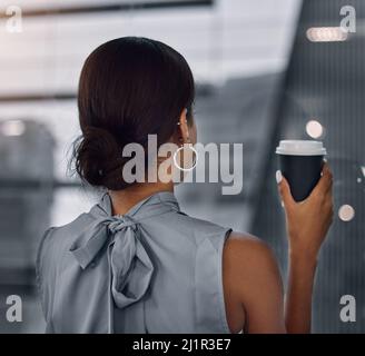 Im in for a long night. Shot of an unrecognizable businesswoman standing alone in the office and having a coffee in the evening. Stock Photo