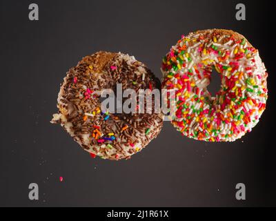 Two sweet colorful donuts in a frozen flight on a gray background. There are no people in the photo. There is free space to insert. Invitation for a h Stock Photo
