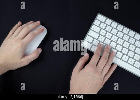 Left-handed woman holds a computer mouse in her left hand. White and silver keyboard on black background Stock Photo