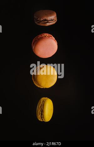 Three french macaroons on a black background in frozen flight. Minimalism. There are no people in the photo. Festive composition. Shop, cafe, confecti Stock Photo
