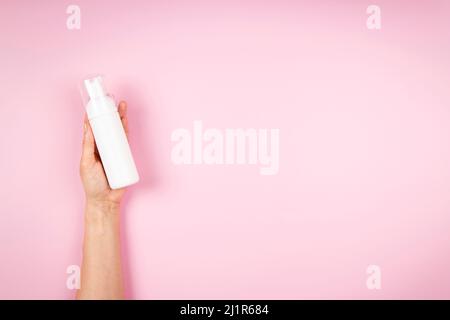 Woman hands holding cosmetic mousse foam bottle on pastel pink background. Blank plastic package container mock up with place for text Stock Photo