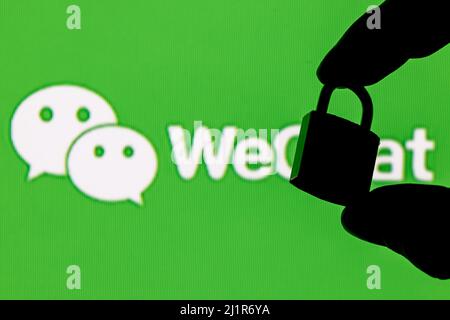 Fingers hold a closed security lock on the background of the WeChat messenger logo. The concept of data security in WeChat. Stock Photo