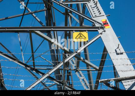 Lower section of a transmission tower with 'Danger of Death' warning sign and climbing proof barbed wire barrier against a blue sky Stock Photo