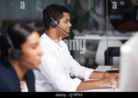 Logging calls and inquiries with a smile. Shot of a young businessman working on a computer in a call centre. Stock Photo