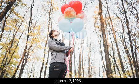 A young handsome man is holding the colorful balloons on walk in autumn forest Stock Photo