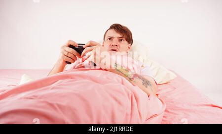 Man with joystick playing video game lying on the bed. A young male with a joystick, gaming addiction Stock Photo