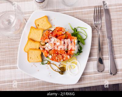 Salmon tartare with avocado garnished with capers, arugula, onion, lemon and toasts Stock Photo