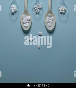 Pills in spoons and scattered on a blue background. Stock Photo