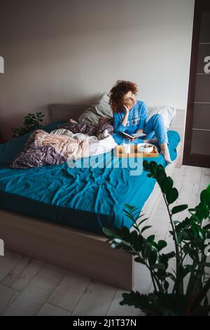 Curly girl sitting in bed looking out the window thoughtfully before eating her healthy breakfast. Healthy lifestyle. Healthy food, diet. Fresh Stock Photo