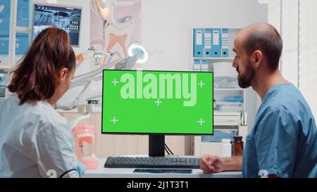 Dentist and man nurse analyzing green screen on computer while looking at teeth scan for oral care in dental office. Dentistry specialists using isolated background and mockup template Stock Photo