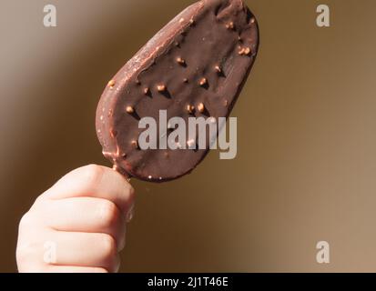 Close-up of a child holding a chocolate ice cream on a stick, on a yellow summer background. Stock Photo