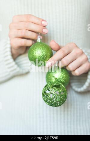 Woman in a light warm woolen sweater holding a toy green balls in her hands, copy space, selective focus. Christmas, new year holiday concept Stock Photo