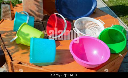 Multicolored empty clean plastic tableware on a wooden background, outdoors, on a sunny summer day. Stock Photo