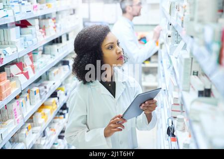 Mobile apps that have pharmacy management covered. Shot of a young woman using a digital tablet to do inventory in a pharmacy. Stock Photo