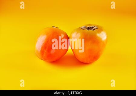 Two Persimmons isolated on yellow background in high resolution Stock Photo