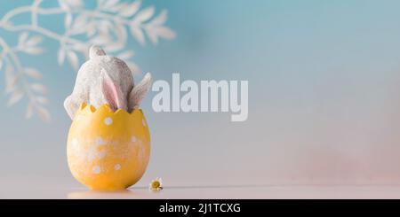 Banner a white rabbit hid in an Easter egg on a blue background. Festive Easter card. Copy space. Stock Photo