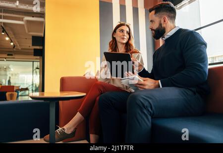 Two young entrepreneurs having an important discussion in an office lobby. Two modern businesspeople using a laptop in a co-working space. Young entre Stock Photo