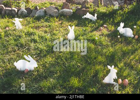 The concept of Easter holidays. Decorative handmade crafts in the form of white rabbits and colorful eggs. Grass in the background. Copy space. Stock Photo