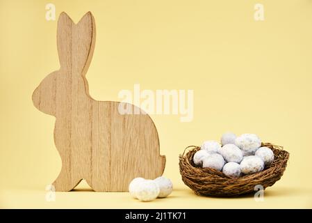 Wooden rabbit and nest with small eggs on yellow background, Happy Easter card Stock Photo