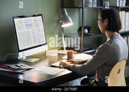 Side view shot of young Asian businessman using computer with data charts while working at home office Stock Photo
