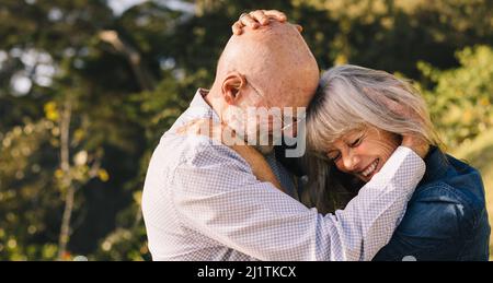 Mature couple touching their heads together while standing outdoors. Happy senior couple sharing a romantic moment in the summer sun. Elderly couple e Stock Photo