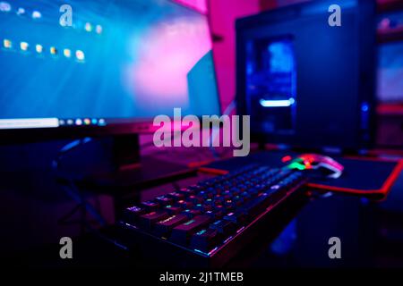 PC with rgb keyboard for gaming computer video games with neon colored background, dark room with game workplace without people Stock Photo