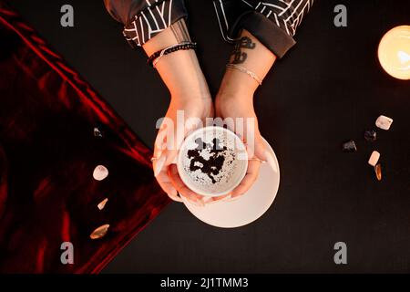 Top down view of female fortune teller holding coffee cup in hands and reading grounds in seance Stock Photo