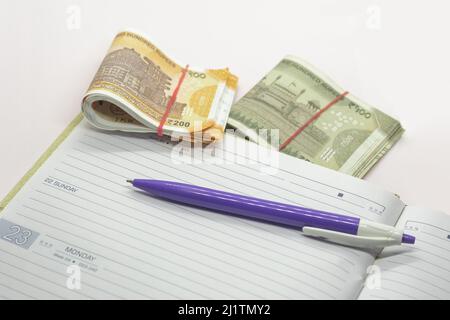 A closeup shot of a purple pen on a notebook and Indian Rupees isolated on a white background Stock Photo