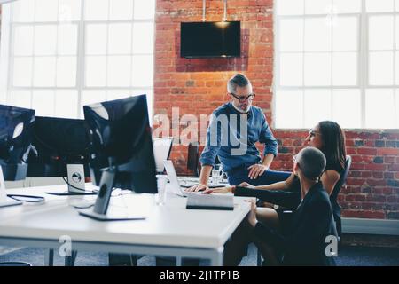 Three businesspeople having a discussion while working together in an office. Group of businesspeople working on a project in a modern workplace. Coll Stock Photo