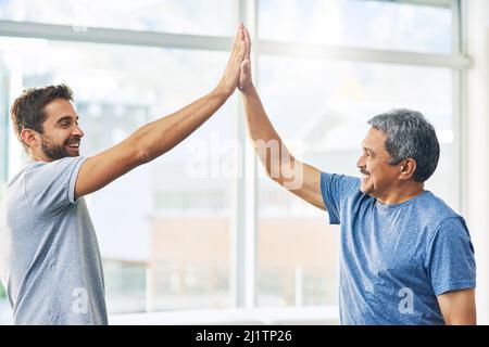 Well done. Cropped shot of a young male physiotherapist and his senior patient high fiving after a great session. Stock Photo