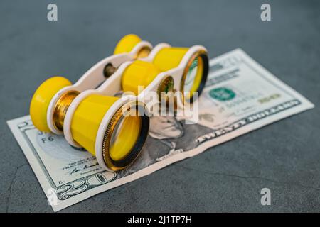 An old theatrical binoculars lies on top of a twenty dollar bill, symbolizing the depreciation of the currency in the world market Stock Photo