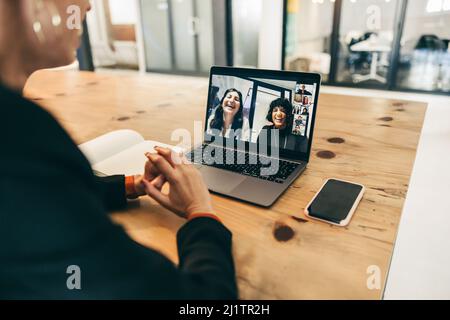 Happy businesswoman attending a video conference in an office. Young businesswoman using a laptop for a virtual meeting with her global partners. Fema Stock Photo