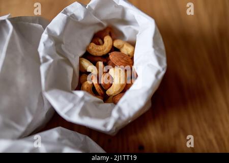 Top view cashew and  almond nuts on the table in a paper bag on wooden background, shopping grocery concept,  nuts delivary,  Zero Waste Food Shopping Stock Photo