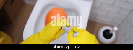 Hands in gloves hold a plunger at the toilet, close-up Stock Photo